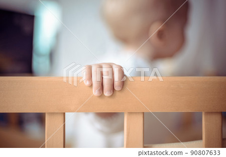 Child's hand on a crib closeup. Baby is standing in his crib and looking away. Child's hand on a crib closeup. Baby is standing in his crib and looking away. 90807633