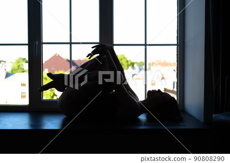 Relaxed Caucasian girl lies by the window. Beautiful female body. Healthcare, diet, sport and fitness. Back lit. Silhouette Relaxed Caucasian girl lies by the window. Beautiful female body. Healthcare, diet, sport and fitness. Back lit. Silhouette 90808290