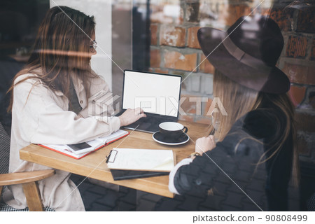 Focused females with laptop sitting at table in cafeteria 90808499