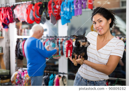 Oriental woman with little dog in salesroom of pet shop Oriental woman with little dog in salesroom of pet shop 90809282