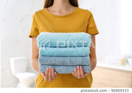 Woman holding fresh towels in bathroom, closeup Woman holding fresh towels in bathroom, closeup 90809315