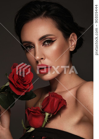 Beautiful brunette woman iwith a classic make-up, red lips, holding flowers. The beauty of the face. 90809444
