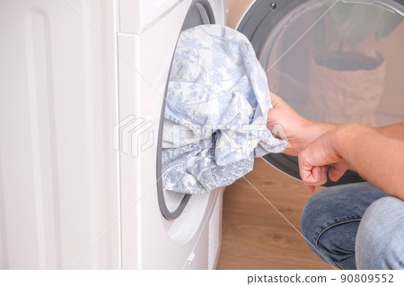 A man takes dried bed linen out of the dryer A man takes dried bed linen out of the dryer 90809552