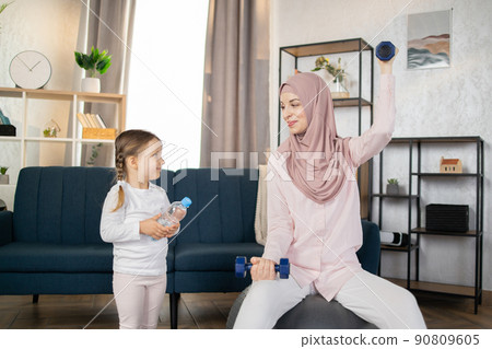Front view of a Muslim mother and little daughter doing sports in morning at home. 90809605