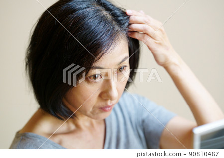 一個穿著T恤的中年婦女,在鏡子裡看著自己的頭髮 一個穿著T恤的中年婦女,在鏡子裡看著自己的頭髮 90810487