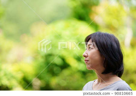 一個穿著T卹，在綠色中孤獨地微笑著的中年婦女 90810665