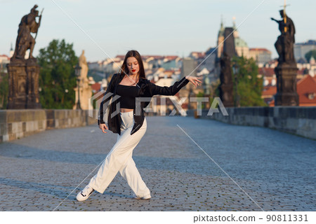 Young woman in casual stylish clothes dancing on the stone bridge of old town in a Prague. Active lifestyle and dancing concept. 90811331
