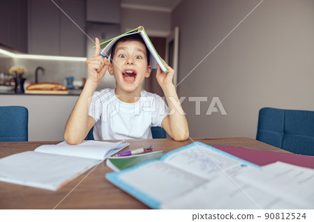 Funny cute smart Caucasian boy holding textbook above head. Having idea. Know solution. Funny cute smart Caucasian boy holding textbook above head. Having idea. Know solution. 90812524