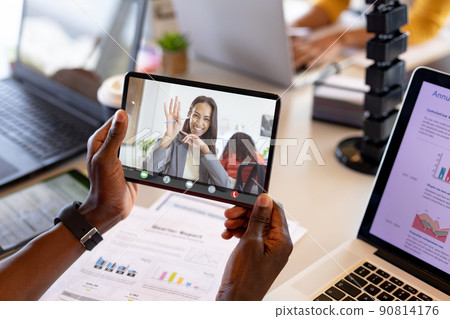 Smiling businesswoman waving at african american businessman seen on digital tablet's display Smiling businesswoman waving at african american businessman seen on digital tablet's display 90814176