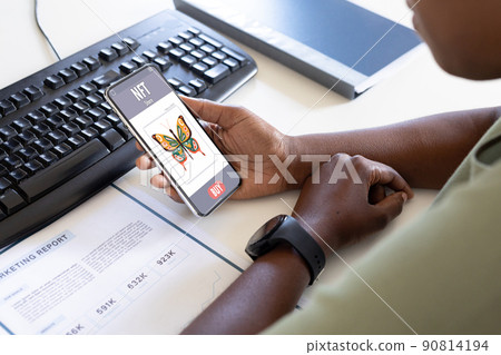 African american businessman studying report while checking nft on smart phone in office African american businessman studying report while checking nft on smart phone in office 90814194