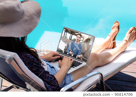 Caucasian young woman video calling male coworker through laptop on poolside during vacation 90814706