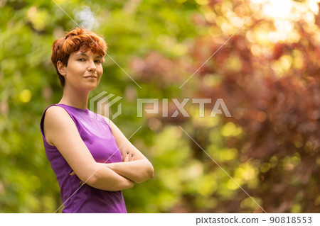 Androgynous woman with crossed arms in park Androgynous woman with crossed arms in park 90818553