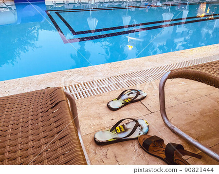 beach supplies are by the pool. nearby are sunbeds for tourists, tables. on the tile sandals, flip flops and people's shoes beach supplies are by the pool. nearby are sunbeds for tourists, tables. on the tile sandals, flip flops and people's shoes 90821444