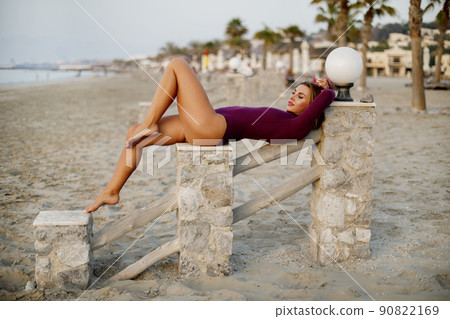 A sexy fit woman in a bodysuit lies on the railing on the beach A sexy fit woman in a bodysuit lies on the railing on the beach 90822169