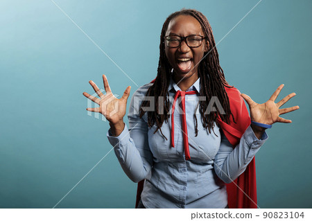 Young adult justice defender wearing red cape yelling in fear at camera while standing on blue background. Scared frustrated superhero woman screaming with mouth wide open. Studio shot Young adult justice defender wearing red cape yelling in fear at camera while standing on blue background. Scared frustrated superhero woman screaming with mouth wide open. Studio shot 90823104