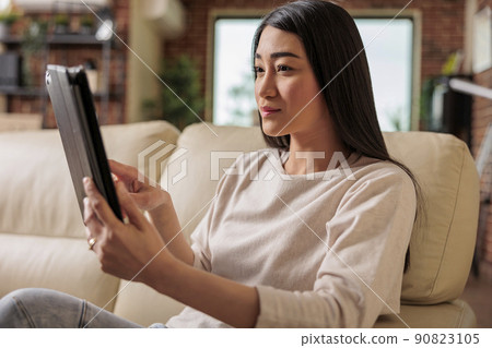 Beautiful young chinese woman using digital tablet at home, connecting internet web 3.0 smiling while sitting on couch entertainment device, browsing internet wireless device computer tablet using Beautiful young chinese woman using digital tablet at home, connecting internet web 3.0 smiling while sitting on couch entertainment device, browsing internet wireless device computer tablet using 90823105