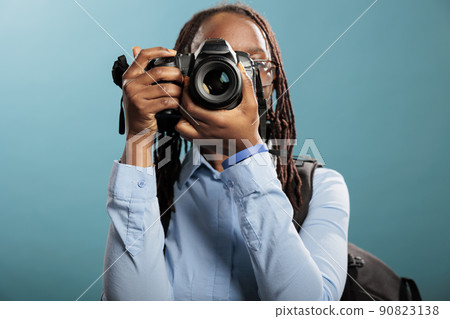 African american young adult photography entusiast with modern photographing device taking photos on blue background. Confident and creative photographer taking pictures while enjoying leisure time. 90823138