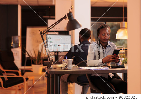 Young businesswoman looking at smartphone app to plan presentation, using social media website to create email report. Analyzing online data on mobile phone to do paperwork research. 90823323