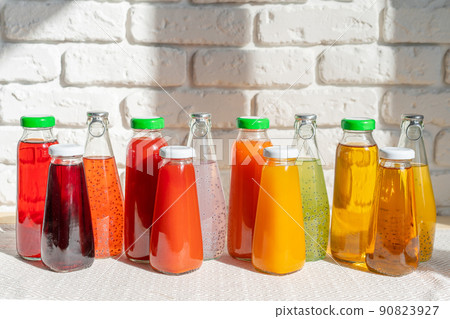 Row of glass bottles of different juices against white brick wall 90823927