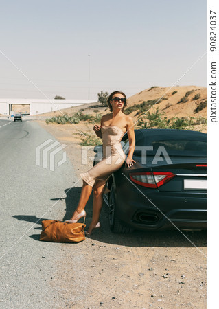 A beautiful sensual girl with blonde hair in an elegant dress posing in the desert near a car A beautiful sensual girl with blonde hair in an elegant dress posing in the desert near a car 90824037