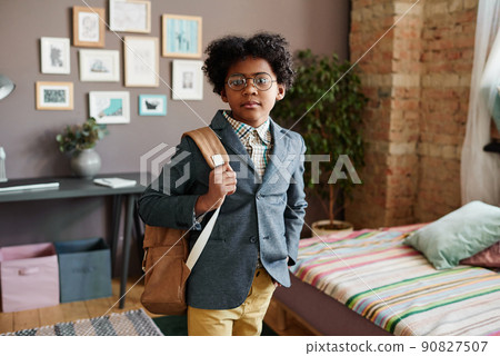 Portrait of African schoolboy in suit with schoolbag looking at camera while standing in room, he going to school in his first time 90827507