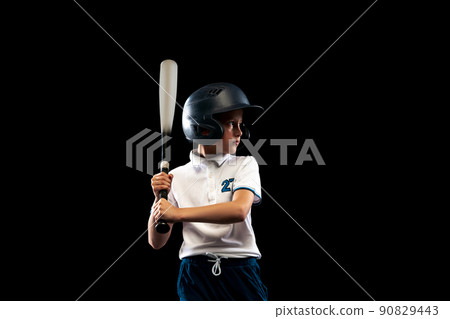 Dynamic portrait of little baseball player, pitcher in blue-white uniform training isolated on black studio background. Concept of sport, achievements, studying, competition 90829443
