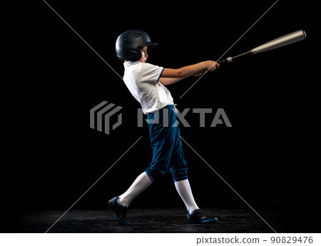 Dynamic portrait of little baseball player, pitcher in blue-white uniform training isolated on black studio background. Concept of sport, achievements, studying, competition 90829476