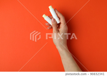 Female hands hold hygienic lipsticks on orange background Female hands hold hygienic lipsticks on orange background 90832341