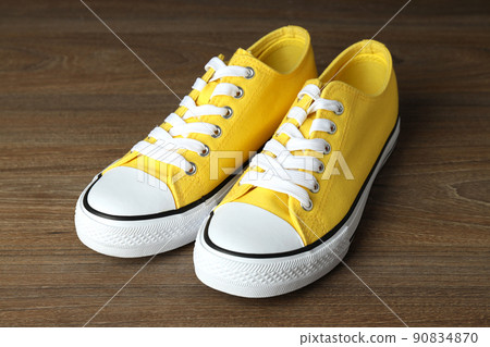 Pair of yellow sneakers on wooden background 90834870