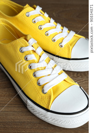 Pair of yellow sneakers on wooden background 90834871
