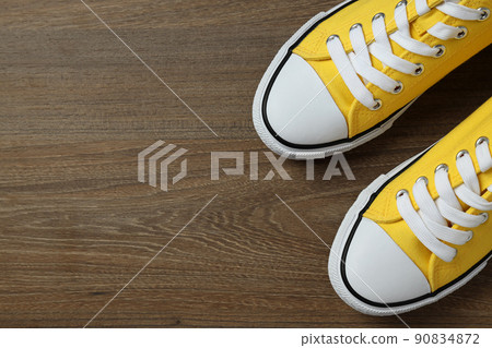 Pair of yellow sneakers on wooden background 90834872