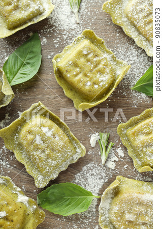 Raw ravioli with flour and basil on wooden background Raw ravioli with flour and basil on wooden background 90835073
