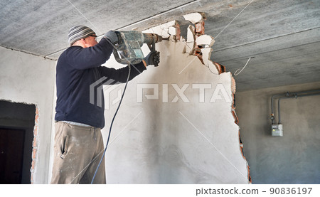 Man builder drilling wall with electric hammer drill. Male worker using professional drilling tool while breaking wall in apartment during renovation. Concept of home renovation and reconstruction. Man builder drilling wall with electric hammer drill. Male worker using professional drilling tool while breaking wall in apartment during renovation. Concept of home renovation and reconstruction. 90836197