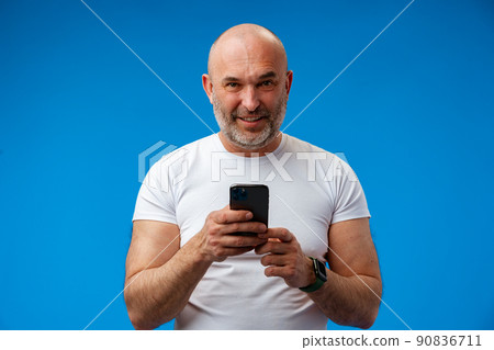 Happy middle-aged man with a phone in his hands against blue background Happy middle-aged man with a phone in his hands against blue background 90836711