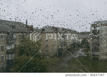 A lot of raindrops on the glass against the background of a cloudy street and blurred houses 90837167