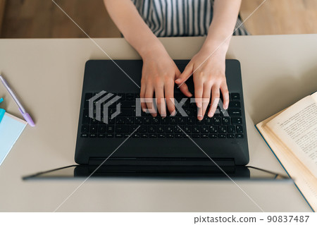 Close-up top view of unrecognizable child school girl typing on laptop keyboard, learning distantly at home, doing home task sitting at table. Pupil schoolgirl e-learning online using computer. Close-up top view of unrecognizable child school girl typing on laptop keyboard, learning distantly at home, doing home task sitting at table. Pupil schoolgirl e-learning online using computer. 90837487