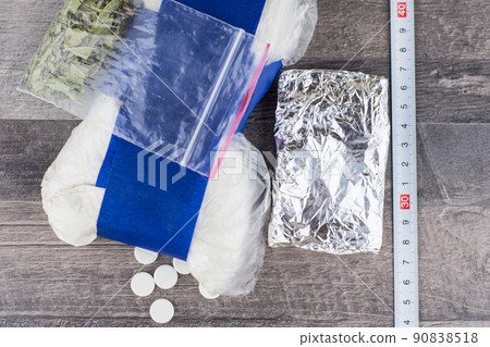 suspected drug trafficking, unknown pills, white powder in a transparent package and the foil, and like a "spice" blend, are on the table, a ruler for measuring on the right suspected drug trafficking, unknown pills, white powder in a transparent package and the foil, and like a "spice" blend, are on the table, a ruler for measuring on the right 90838518