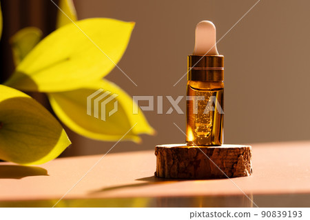 Cosmetic amber glass dropper bottle on wooden podium with oil, serum or fruit peeling in the sunlight. Green ruscus, soft focus. Beauty product presentation, natural background. Front. Mockup concept  90839193