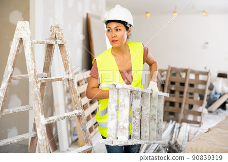 Woman builder carrying stepladder 90839319