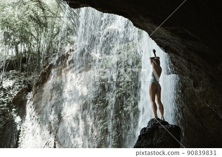 Woman sit on rock under waterfall in tropical jungle Woman sit on rock under waterfall in tropical jungle 90839831