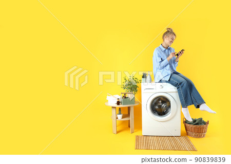 Concept of housework with washing machine and girl on yellow background Concept of housework with washing machine and girl on yellow background 90839839