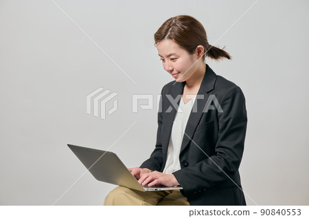 A young woman in a jacket operating a computer on her lap 90840553