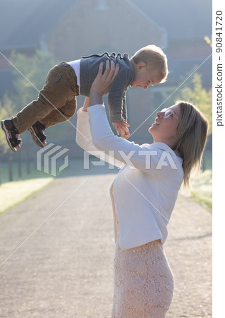 a young and happy mother and child, playing, stands in the middle of a park in the rays of the a young and happy mother and child, playing, stands in the middle of a park in the rays of the 90841720