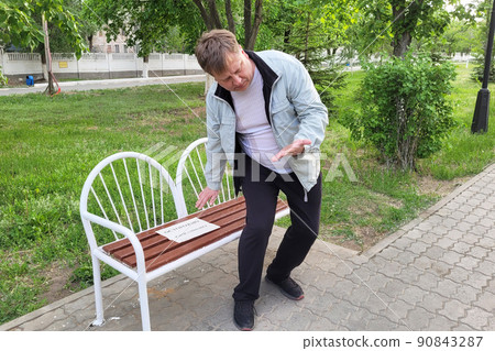 An adult man soiled his clothes and hands on a painted bench in the park. The inscription on the paper is carefully colored 90843287