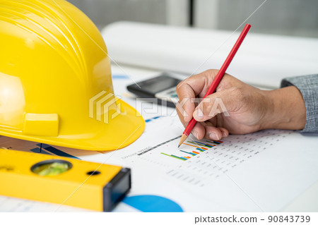 Asian engineer with plan project blueprint, graph and yellow helmet and engineering construction tools. Asian engineer with plan project blueprint, graph and yellow helmet and engineering construction tools. 90843739