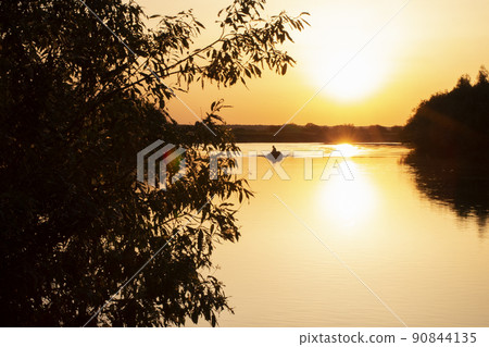 Sunset on the lake among the trees and in the distance a boat with a fisherman. 90844135