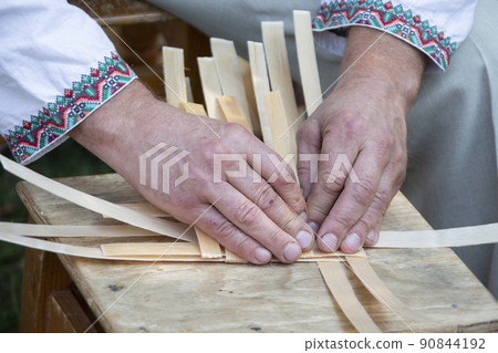 The hands of the master weave a basket of birch vines. 90844192