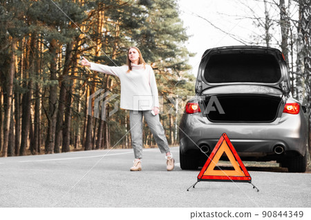 Red emergency triangle with blurred car and woman calling car mechanic in the background. Accident and broken car on the road. Selective focus. Red emergency triangle with blurred car and woman calling car mechanic in the background. Accident and broken car on the road. Selective focus. 90844349
