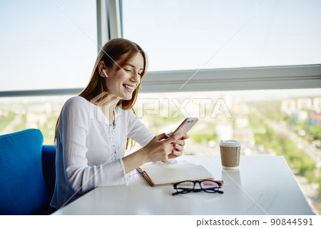 Cheerful student in electronic headphones choosing music songs for listening playlist during free time 90844591