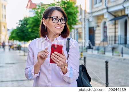 Middle aged smiling woman looking into smartphone on city street 90844689